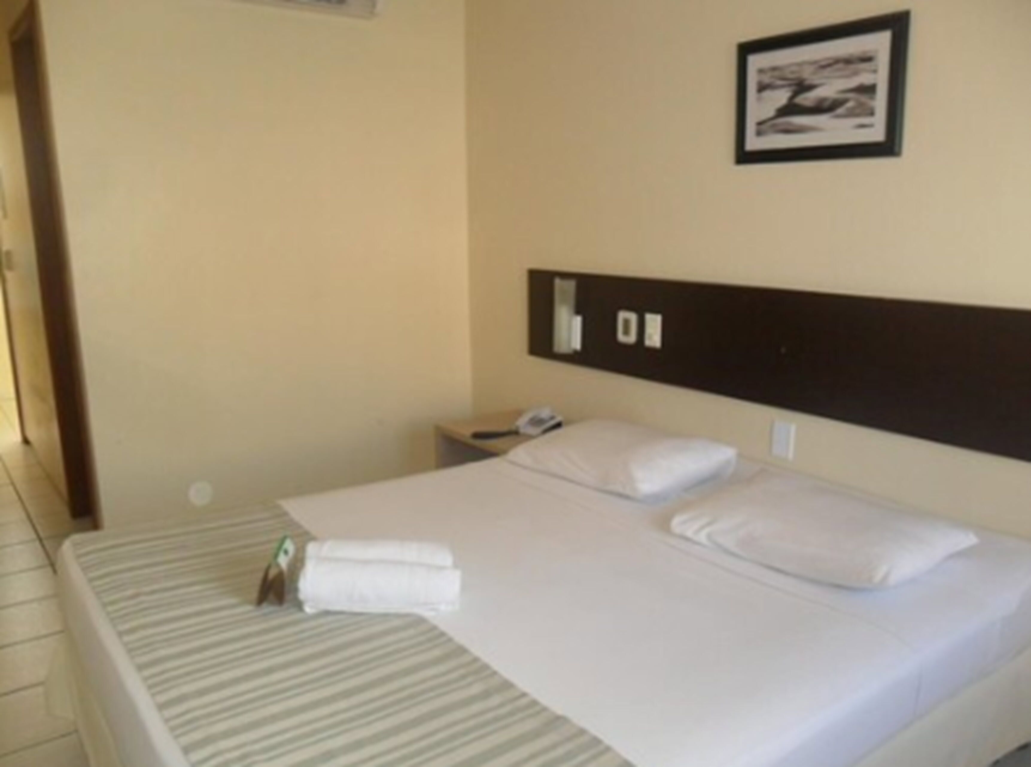 A hotel room with a bed, a nightstand, a phone, and a framed picture on the wall.