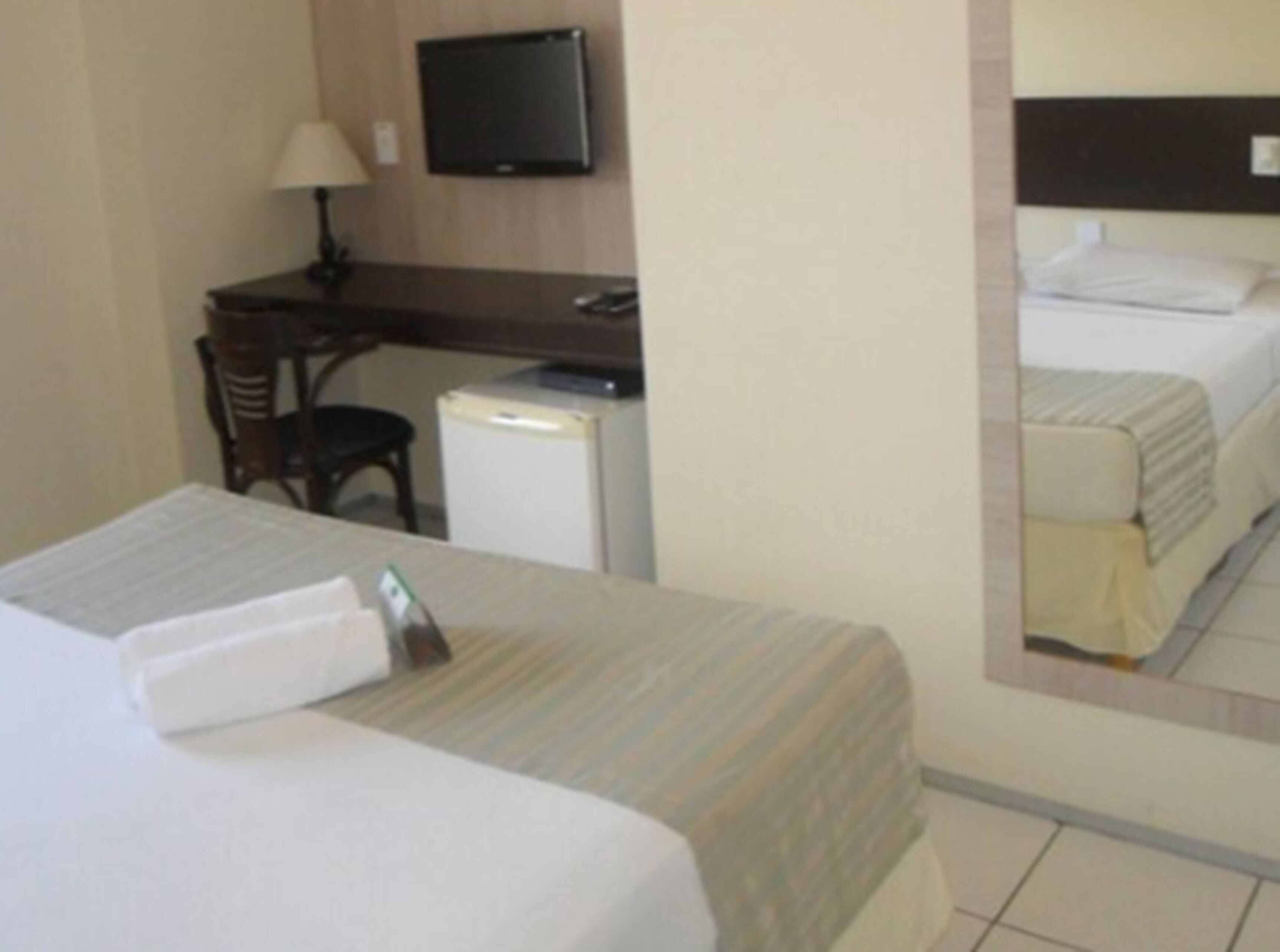 A hotel room with a bed, a desk, a chair, a television, and a small refrigerator.