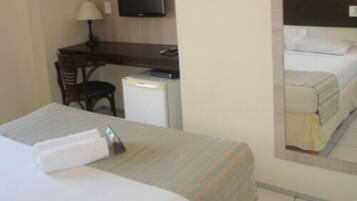 Una habitación de hotel con cama, escritorio, silla, televisión y refrigerador pequeño.