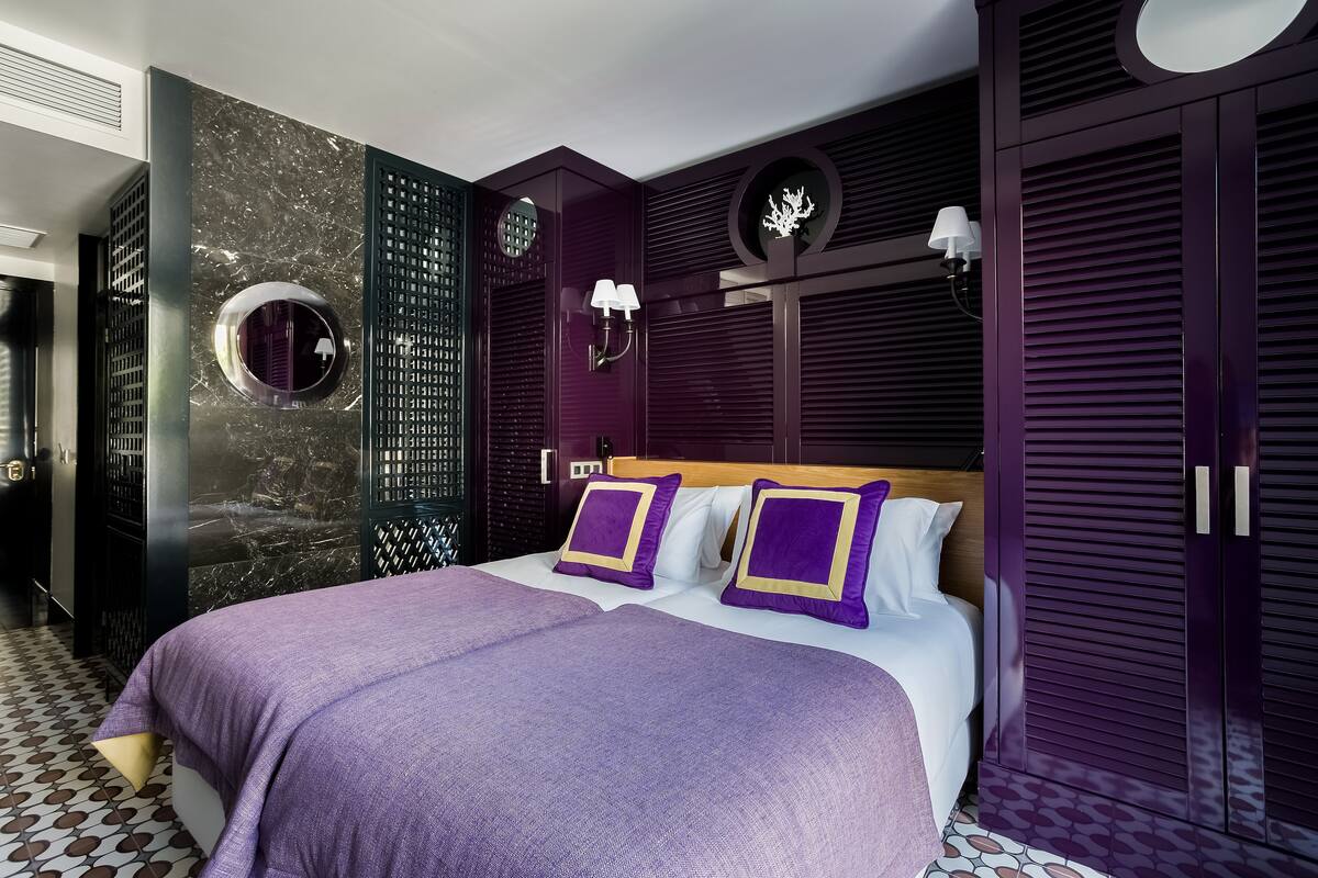 A modern bedroom with a large bed, purple bedding, and a dark wood wardrobe.