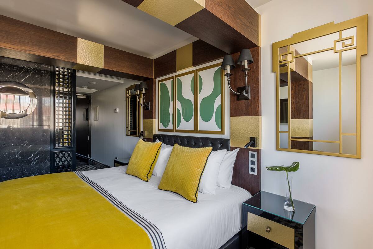 A hotel room with a bed, a nightstand, a mirror, and a decorative wall panel.