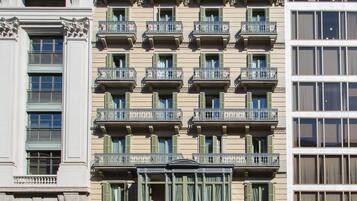 Un hotel de varios pisos con balcones, un letrero llamativo que dice "NOVA OBTURADA HOTEL ROOM MATE ANNA" y una señal de calle que indica la dirección a puntos de referencia cercanos.