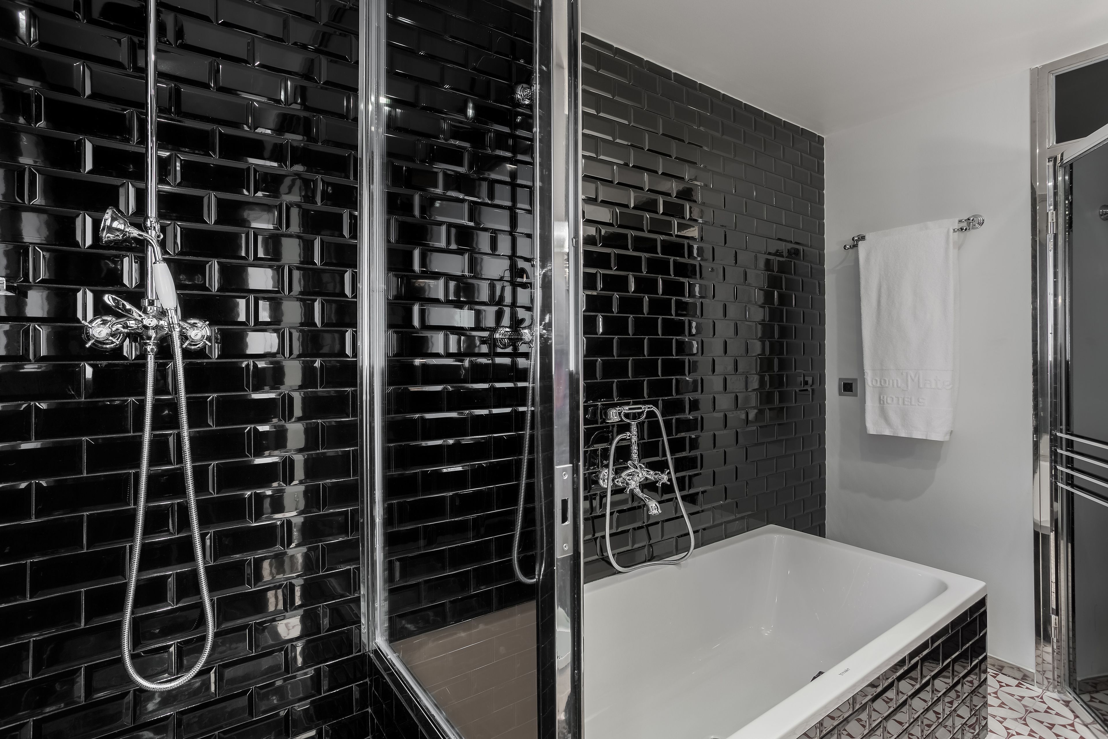 Een moderne badkamer met een zwart betegelde wand, een douche met glazen wanden en een wit bad.
