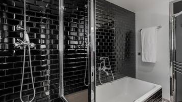 Een moderne badkamer met een zwart betegelde wand, een douche met glazen wanden en een wit bad.