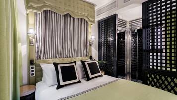 Ein Hotelzimmer mit einem großen Bett, gestreifte Vorhänge, einem gepolsterten Kopfteil und einem schwarzen Sichtschutz.