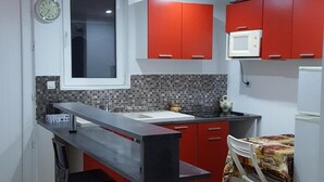 Eine kompakte Küche mit Kochinsel, roten Schränken und einer gefliesten Spritzschutzwand.