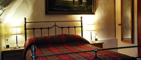 A bedroom with a bed, a nightstand, a lamp, a painting on the wall, and a door.