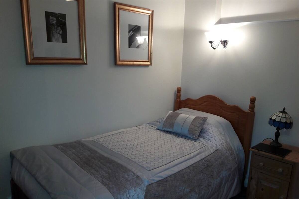 Un dormitorio con cama, dos cuadros en la pared, una lámpara de noche y una mesita de noche.