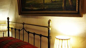 Habitación de hotel con cama, un cuadro de un paisaje, una mesita de noche con lámpara y una botella de agua.