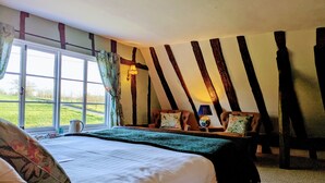 A bedroom with a large bed, two chairs, a window with curtains, and exposed wooden beams. - The Four Horseshoes (Eye)