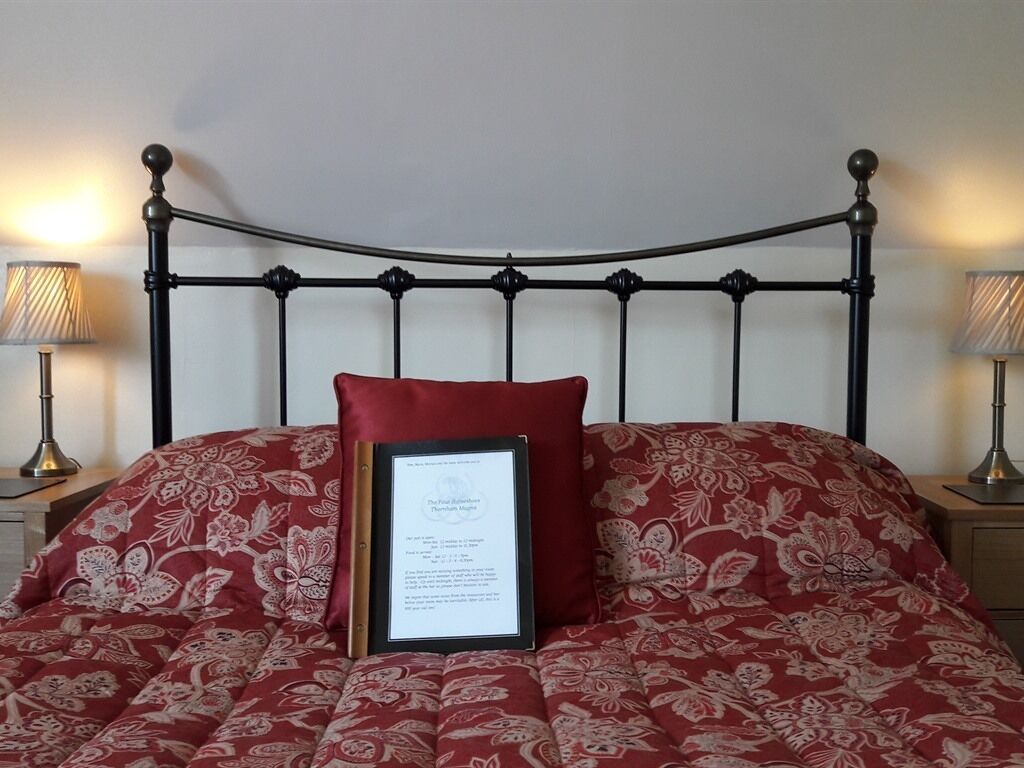 A neatly made bed with a floral-patterned bedspread and a red pillow, a framed certificate on the bed, and two bedside lamps on either side.