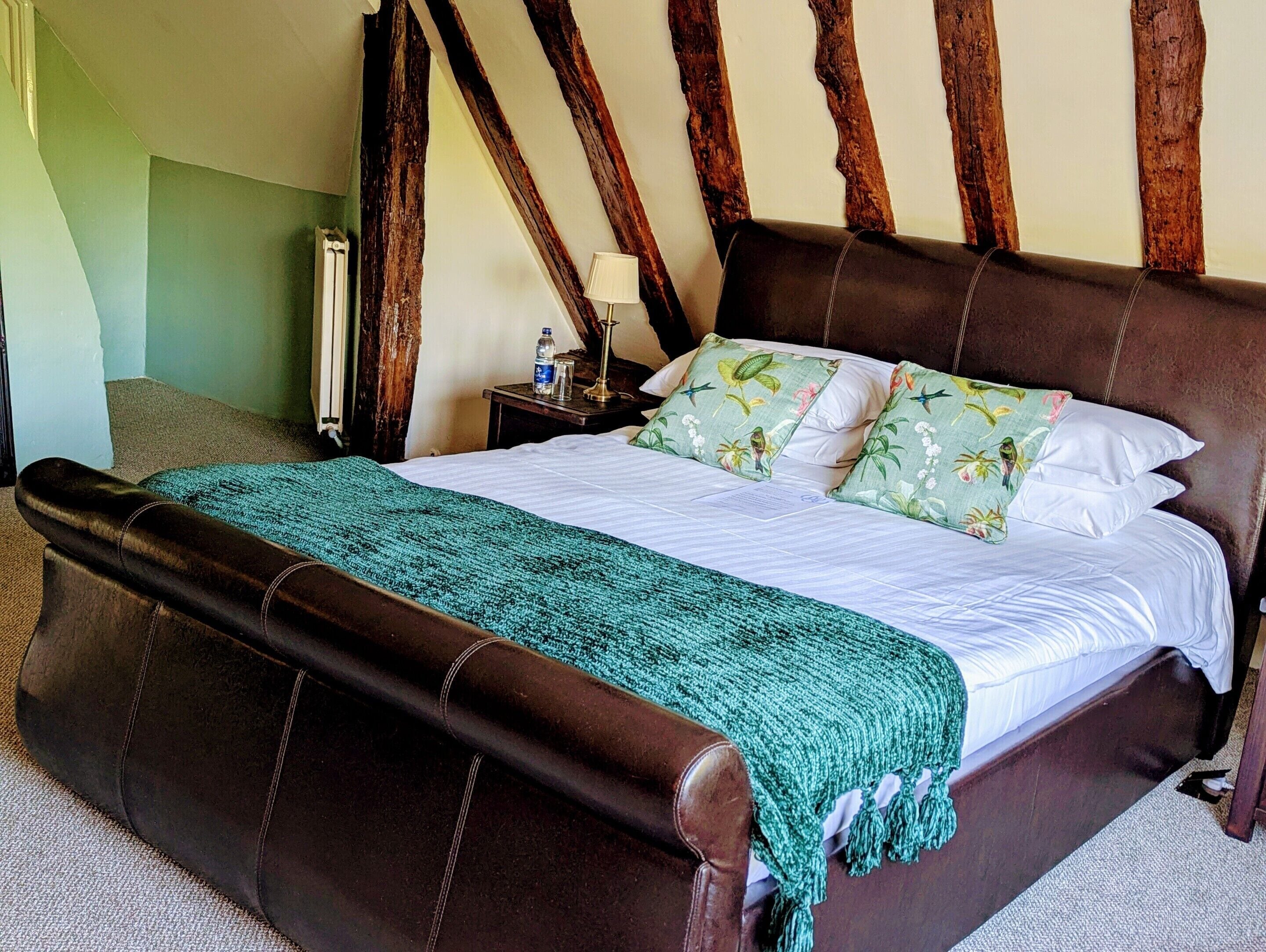 A bedroom with a large bed, a nightstand, a lamp, and a wooden beam ceiling.