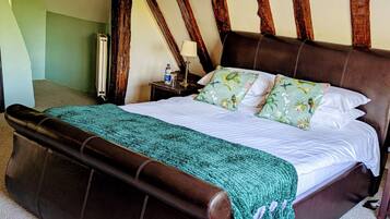 A bedroom with a large bed, a nightstand, a lamp, and a wooden beam ceiling.