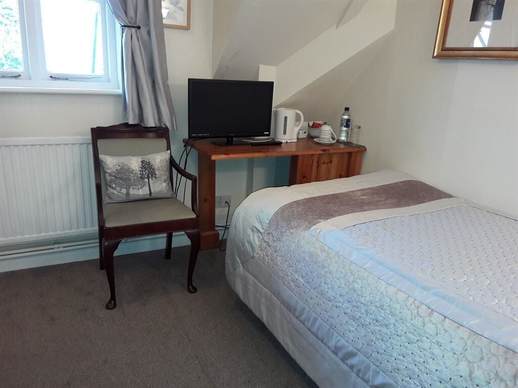 A bedroom with a bed, a desk with a computer, a chair, and a window.