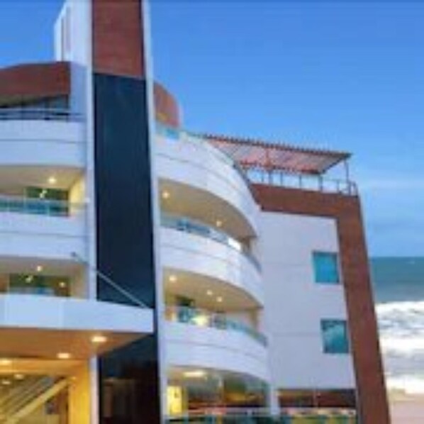 A modern hotel with multiple balconies, a prominent staircase, and a view of the ocean.