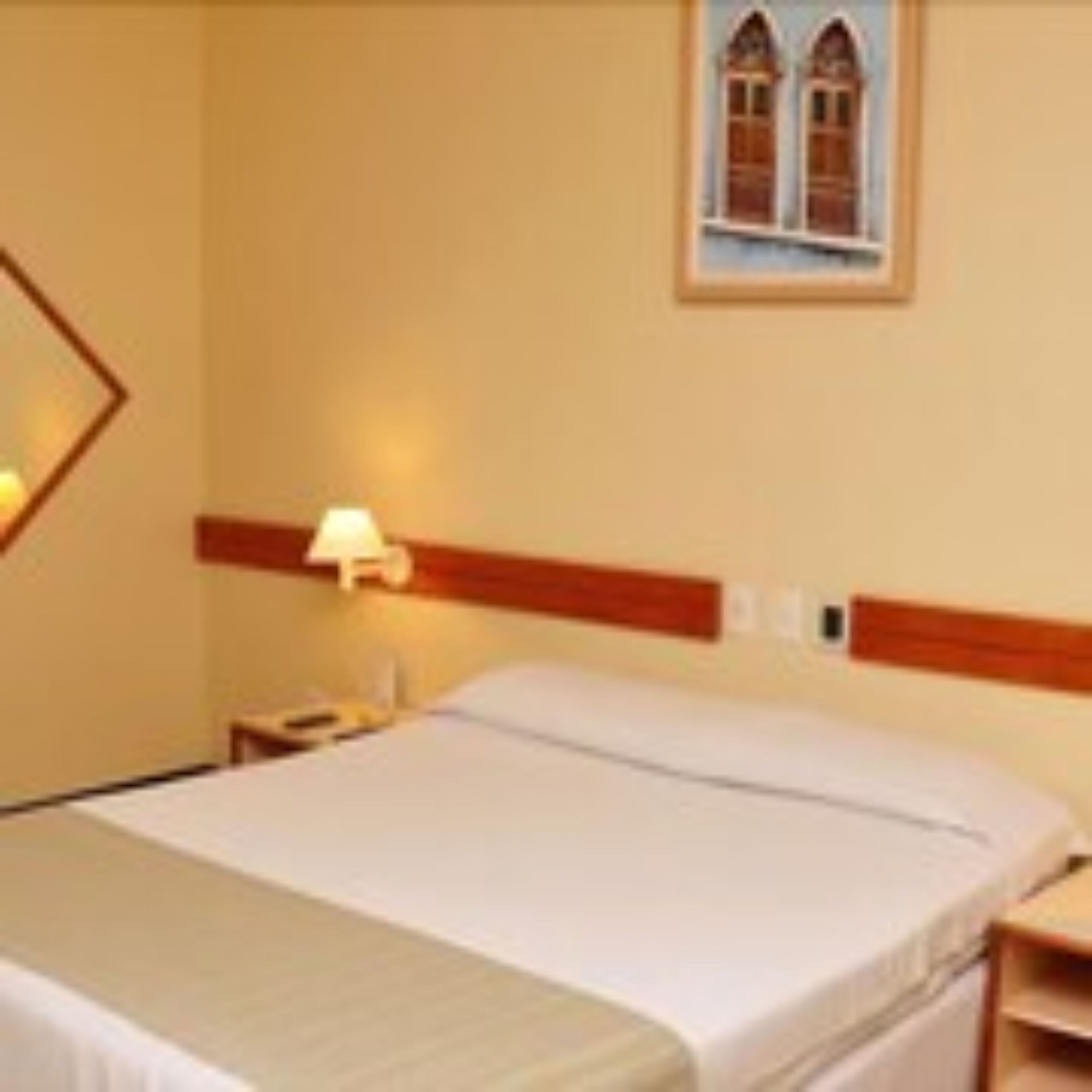 Quarto de hotel com cama, mesa de cabeceira, abajur e janela com vista.