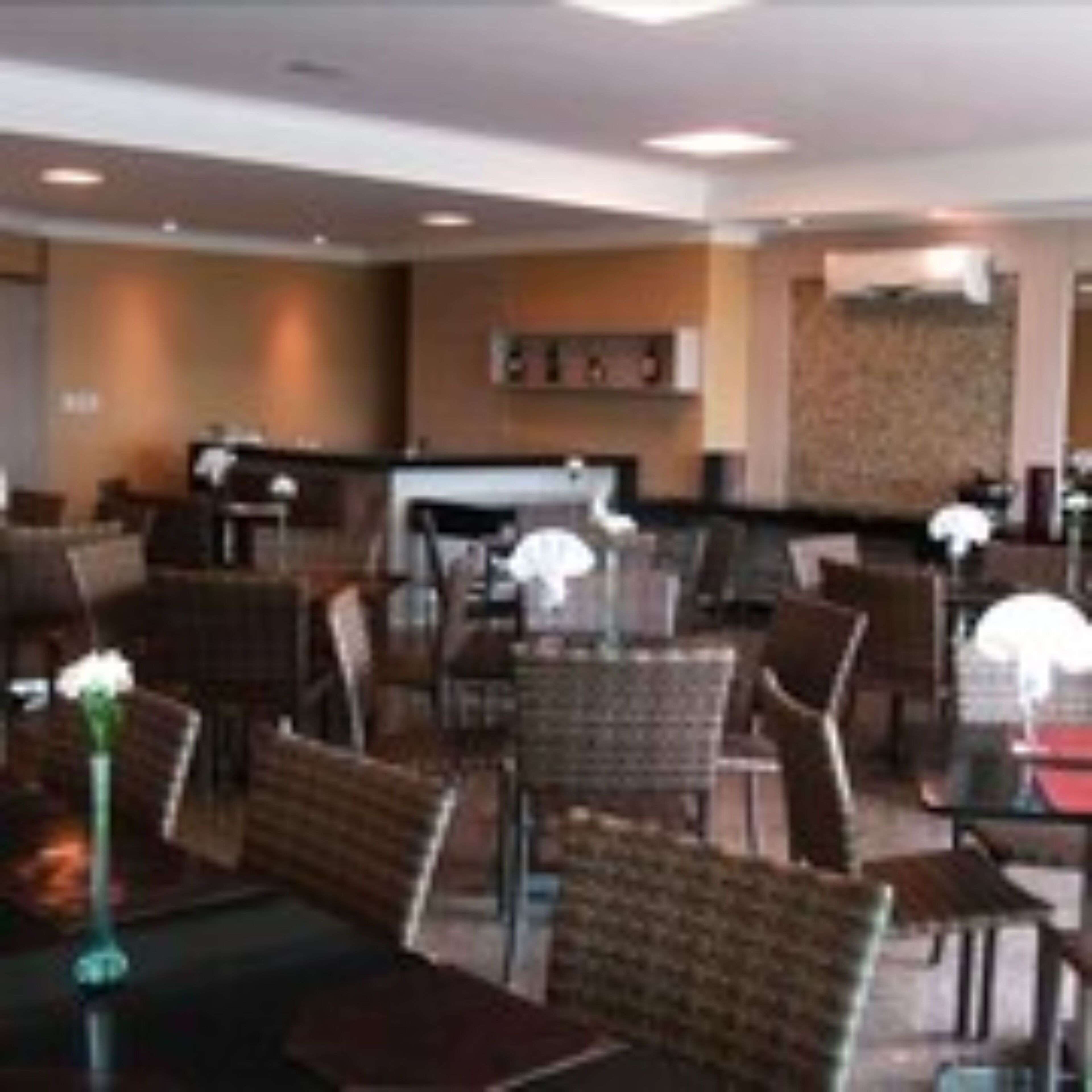 A hotel lobby with multiple seating areas, including tables and chairs. There is a reception desk in the background.