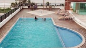A swimming pool with a view of the beach, lounge chairs, and a covered area. - Calhau Praia Hotel (São Luís)