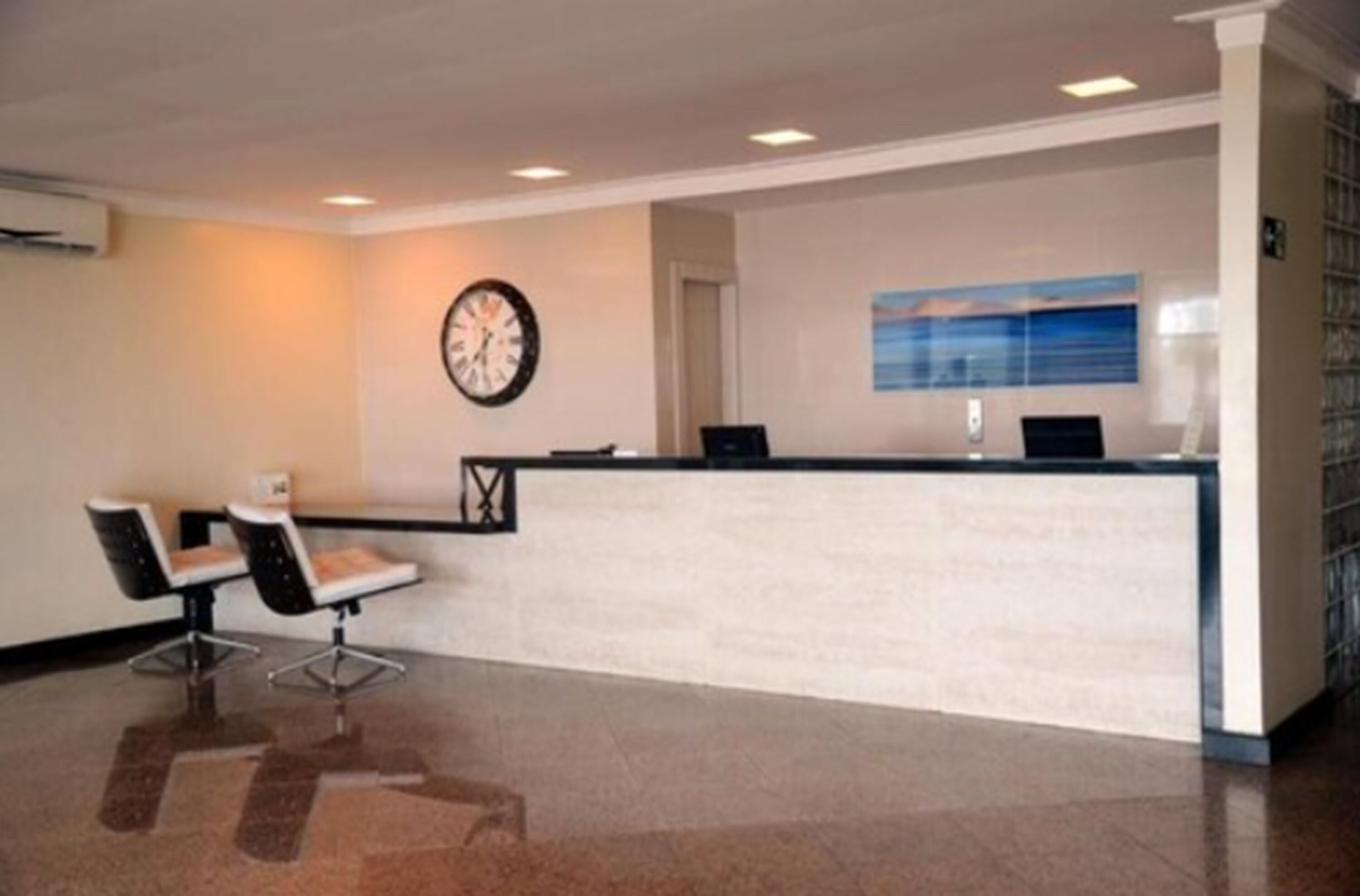 A reception area with a reception desk, two chairs, a clock, and a painting on the wall.