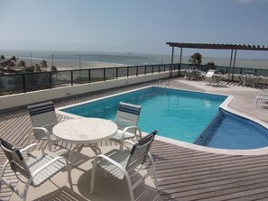 Una piscina en la azotea con vista al océano, rodeada de sillas de descanso y una mesa.