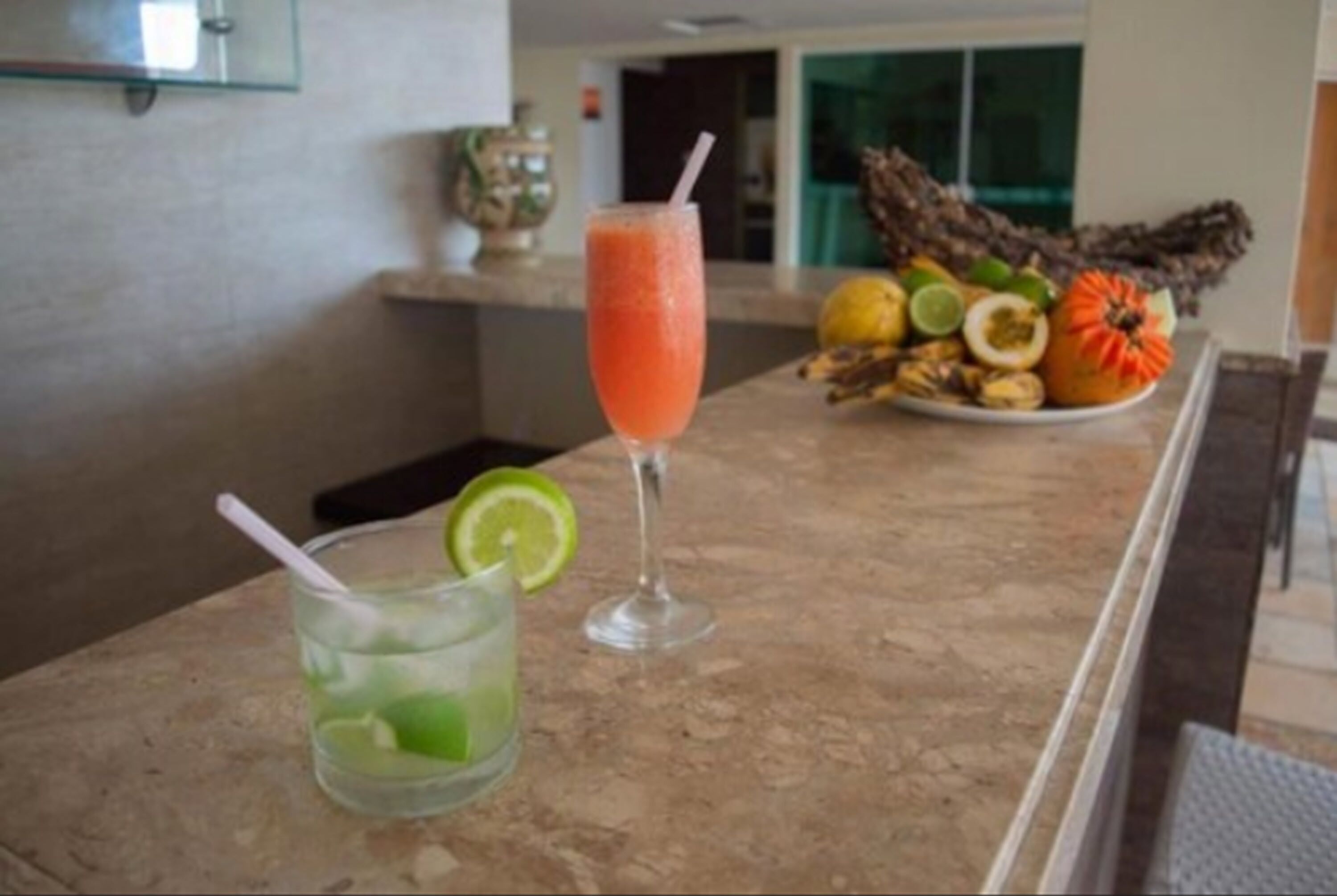 A bar area with a drink in a tall glass and a plate of fruits.