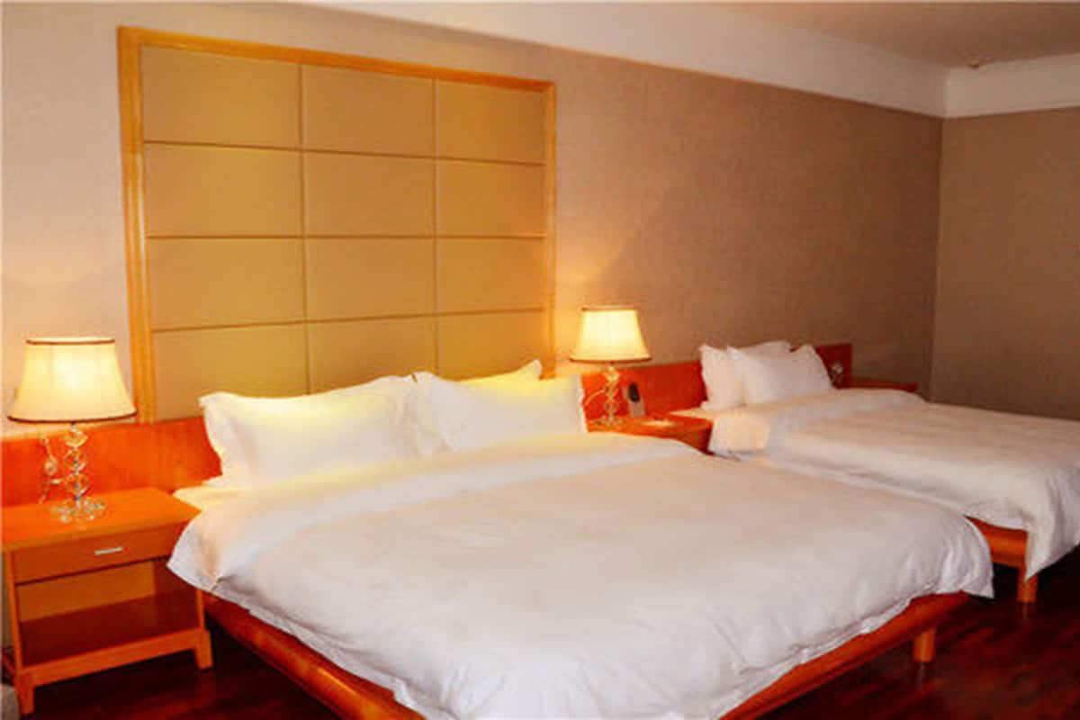Una habitación de hotel con dos camas, un cabecero grande, lámparas de noche y un cuadro en la pared.