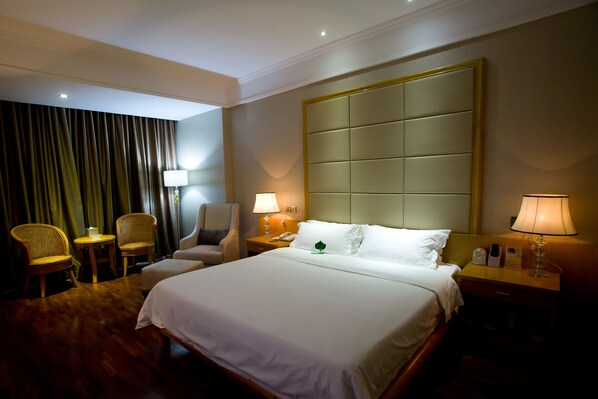 A hotel room with a large bed, two bedside tables, a chair, a lamp, and a curtain. - San Jiang Grand Hotel (Vientiane)