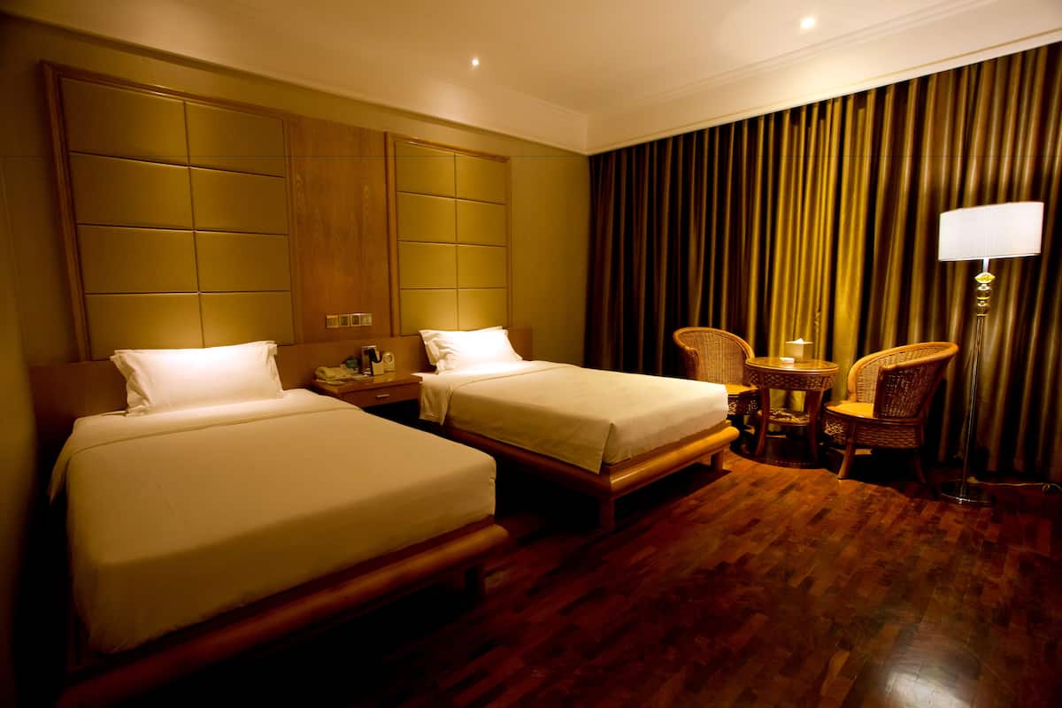 Habitación de hotel con dos camas, un cabecero de madera, una mesita con una silla y una lámpara.