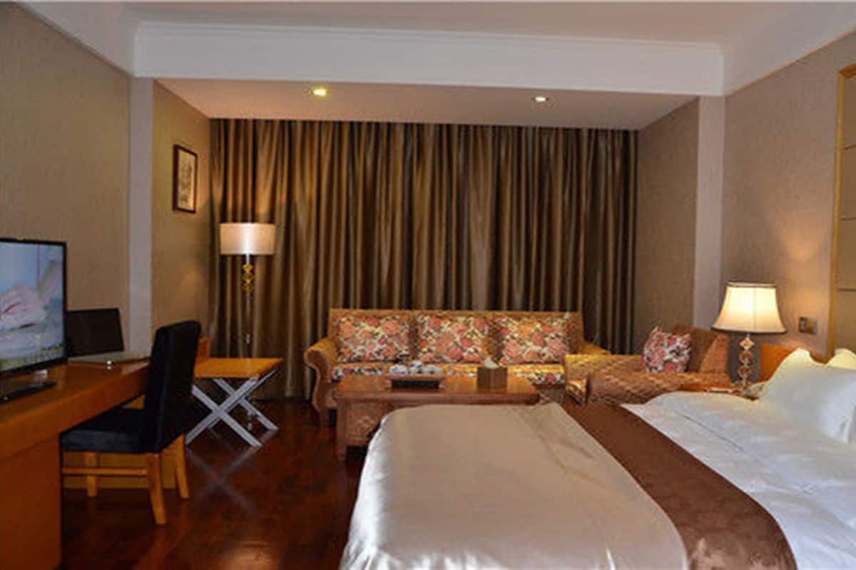 Una habitación de hotel con cama, sofá, escritorio con silla, televisión y lámpara.