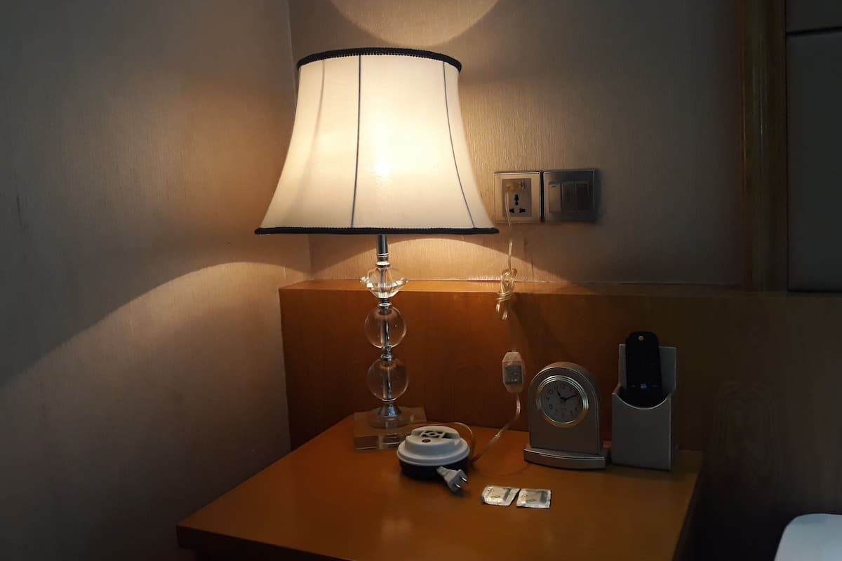 Una habitación de hotel con una mesita de noche que incluye una lámpara, un reloj y un teléfono.