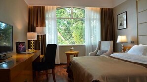 Habitación de hotel con cama, escritorio con silla, televisor y ventana con cortinas.
