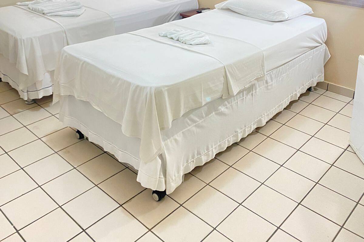 A hotel room with two beds, a wall-mounted air conditioner, and a plain tiled floor.