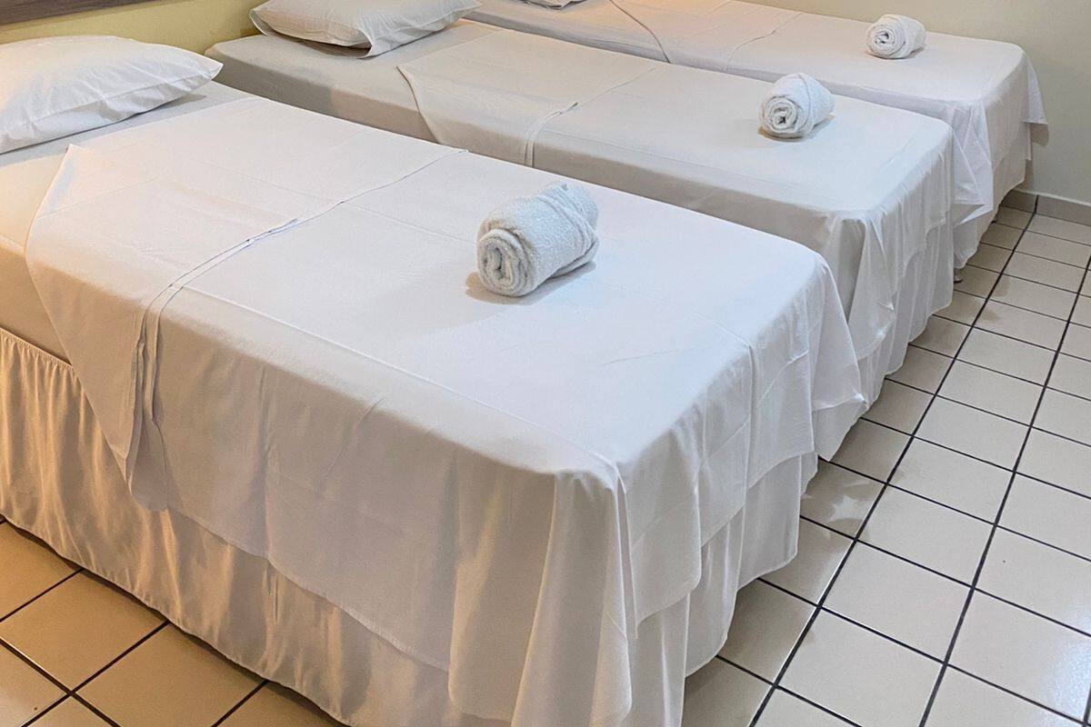 A hotel room with three single beds, a wall-mounted air conditioner, and a light fixture.