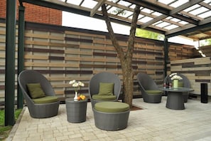 A covered outdoor seating area with wicker furniture and a wooden wall.