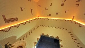 A tiled bathroom with a geometric pattern on the walls and floor, a blue-tiled shower area, and a handrail. - Villa Four Rooms (Kharkiv)