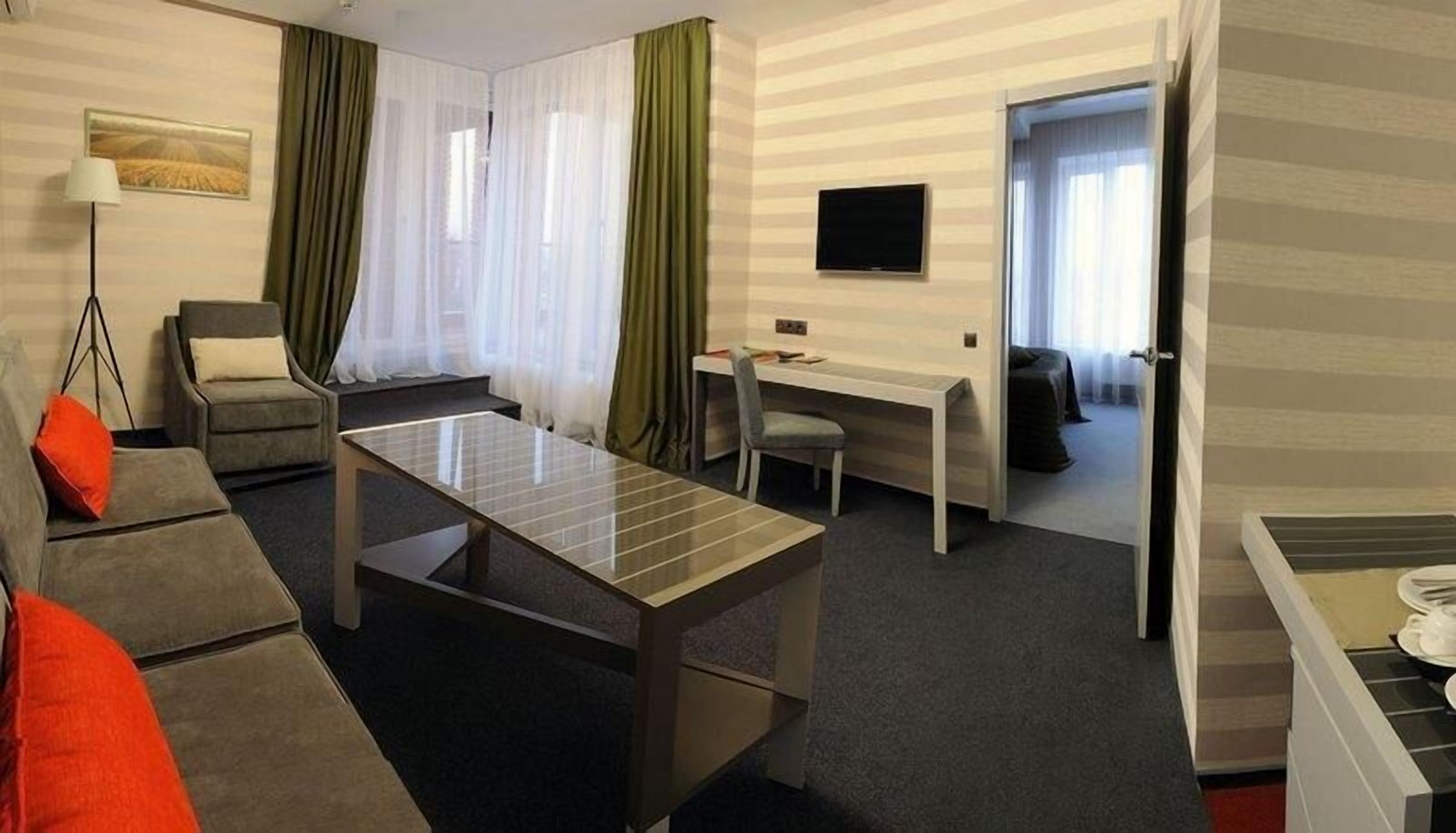 A hotel room with a sofa, a coffee table, a desk, a chair, and a TV.
