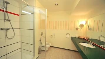 A modern bathroom with a glass shower enclosure, a toilet, a sink with a mirror, and a wall-mounted light fixture.