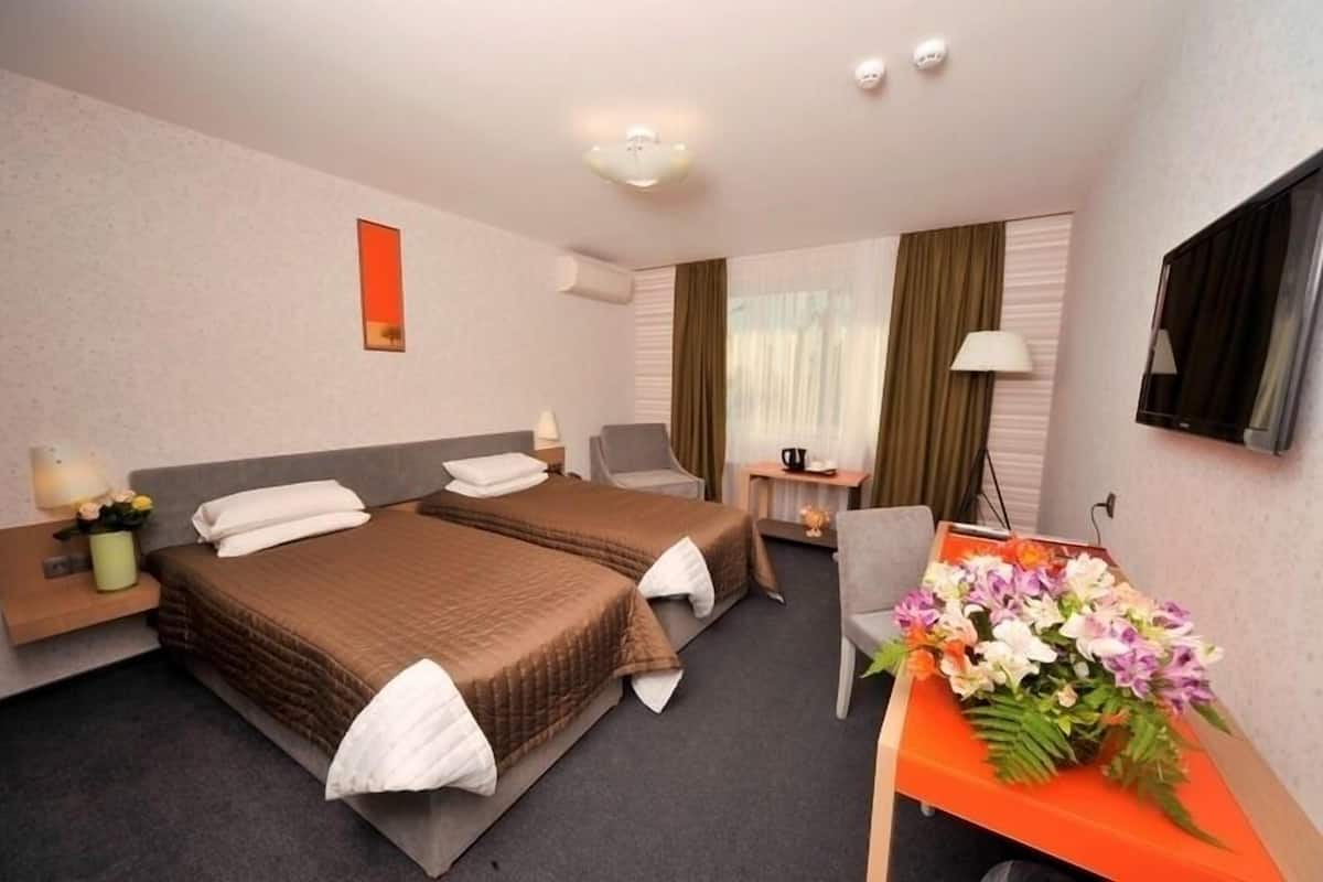 Ein Hotelzimmer mit zwei Betten, einem Schreibtisch, einem Stuhl, einem Fernseher und einem Fenster mit Vorhängen.