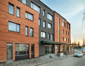 A modern multi-story building with brick and dark grey facades, large windows, and a covered entrance area.