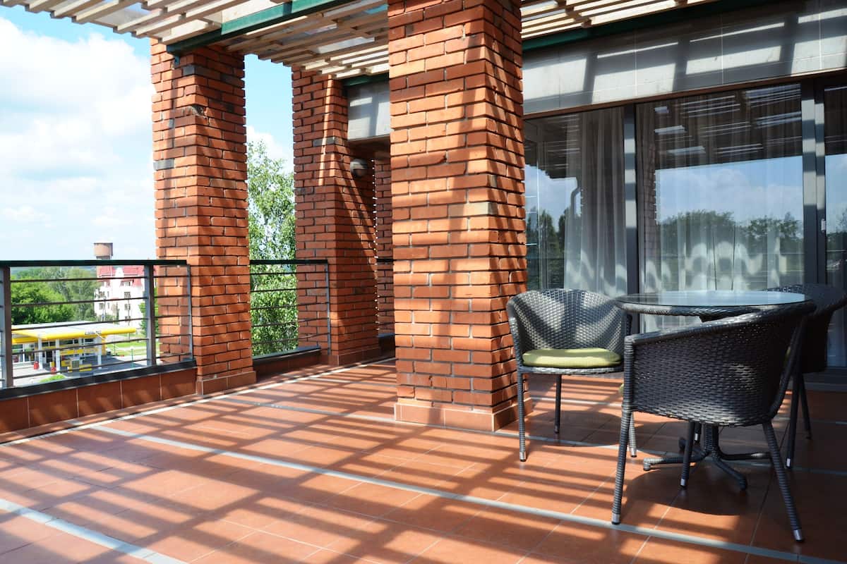 Ein Balkon mit einer Backstein-Säule, einer Glastür und einem runden Tisch mit zwei Korbstühlen.