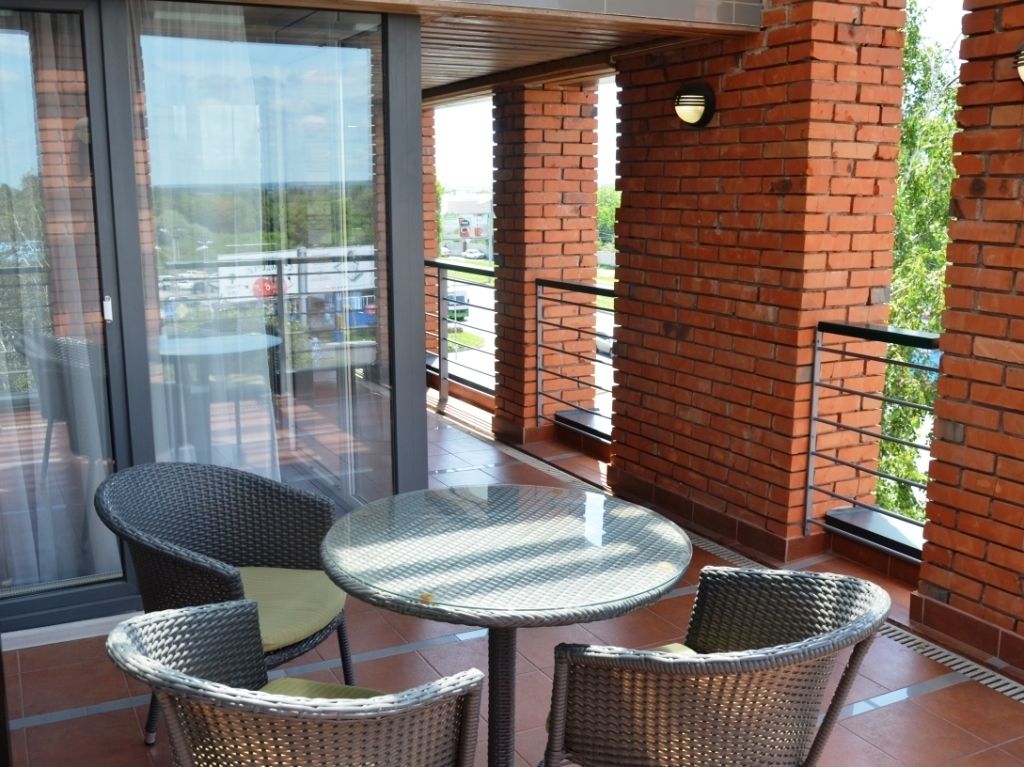 Un balcon avec des fauteuils en osier et une table en verre, des murs en briques et une vue sur l’extérieur.