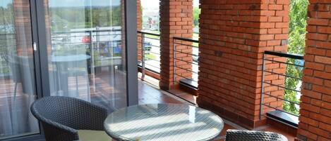 Un balcon avec des fauteuils en osier et une table en verre, des murs en briques et une vue sur l’extérieur.