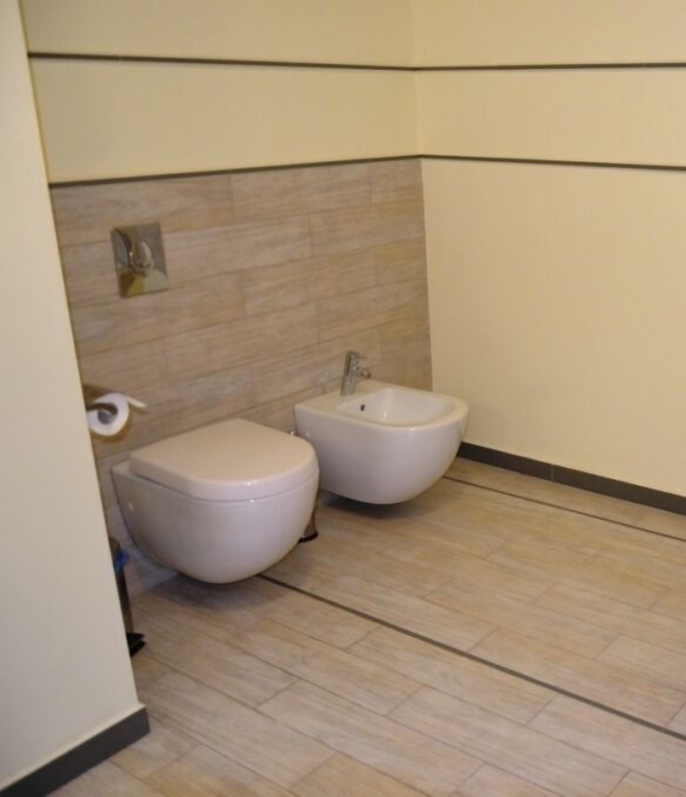 A small bathroom with a toilet and bidet, tiled walls, and a wooden floor.