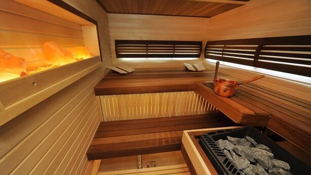 A sauna with wooden benches, a stone wall with a heat source, and a copper bucket. - Villa Four Rooms (Kharkiv)