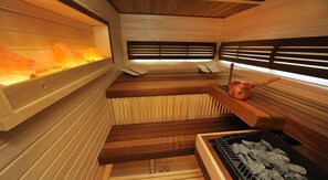 A sauna with wooden benches, a stone wall with a heat source, and a copper bucket. - Villa Four Rooms (Kharkiv)