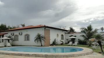 Une maison avec une piscine, entourée de palmiers et sous un ciel nuageux.