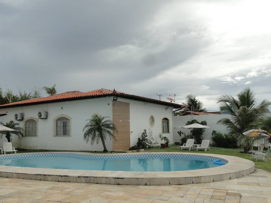Une maison avec une piscine, entourée de palmiers et sous un ciel nuageux.