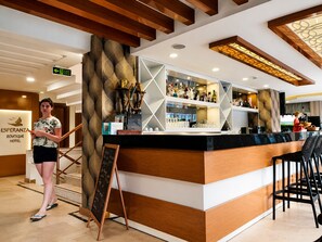 Eine Hotelbar mit Holztresen, einem Schild mit der Aufschrift 'ESPERANZA Boutique Hotel' und einer Person, die am Tresen steht.