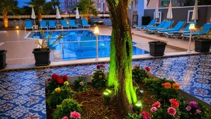 A pool area with lounge chairs, a tree, and potted plants.
