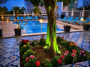 Un área de piscina con sillones de descanso, un árbol y plantas en macetas.